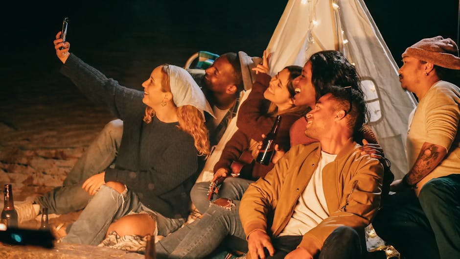 A group of friends joyfully taking a selfie at a nighttime camping gathering by the beach.