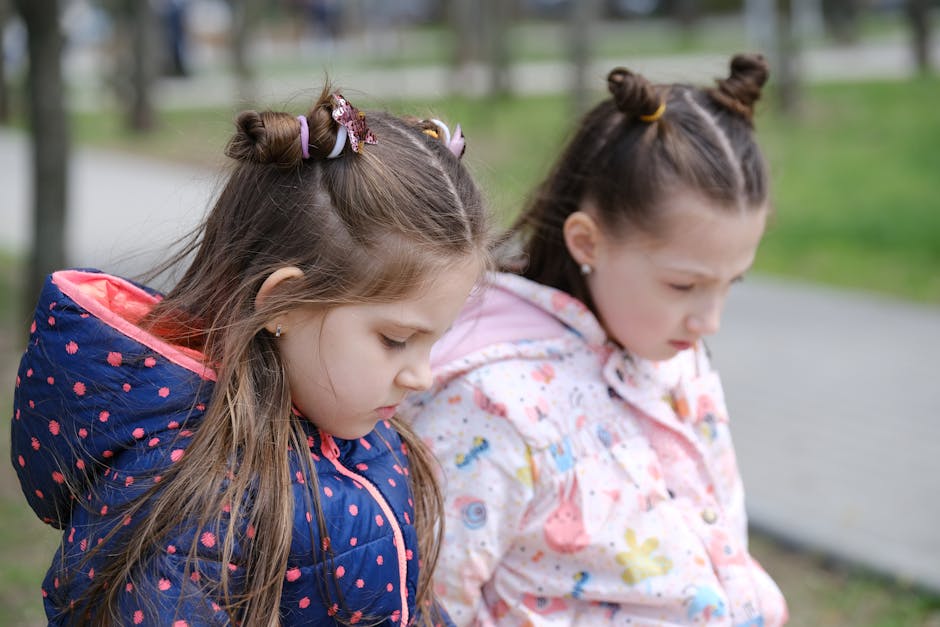 Two young girls in winter jackets, contemplative in a park setting.
