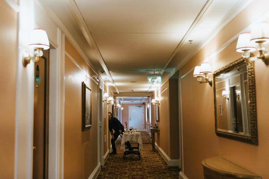 A hotel hallway with a staff member and room service trolley near guest rooms.