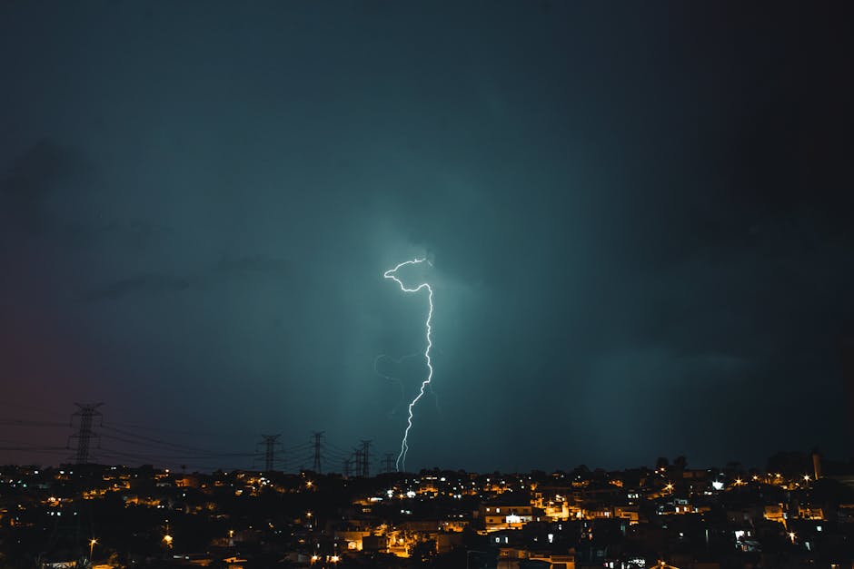 Striking lightning bolt amid dark storm clouds above city skyline, captured at night.