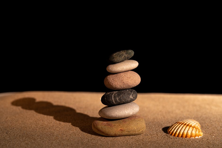 Peaceful zen rock stack with a seashell on a sandy surface, highlighting balance and tranquility.
